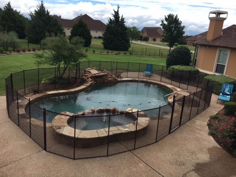Black pool safety fence around a free form pool with rock feature and spa showing traits of a safety fence.
