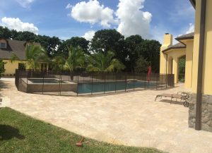 Black pool safety fence around a large pool and spa behind a yellow stucco house in Miami.