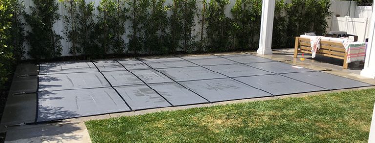 Pool fence Los Angeles installation in a backyard, featuring a safety cover over the pool and a white fence with greenery in the background.