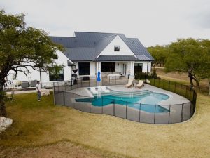 Black mesh pool fence enclosing modern Grecian backyard swimming pool at a farmhouse in Houston, Texas
