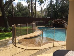 Tan mesh pool fence installation curving around a natural-style pool with waterfall in Houston backyard