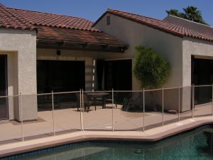 Modern backyard with a pool fence in the Inland Empire, showcasing a patio with outdoor furniture and a small tree near the house.