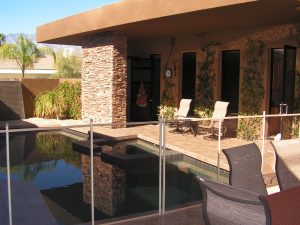 Modern patio with stone pillar and seating, showcasing an Inland Empire pool fence around a pool with a hot tub.