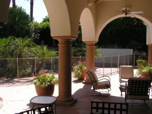 View from a patio with columns and seating, showcasing an Inland Empire pool fence enclosing a garden area.