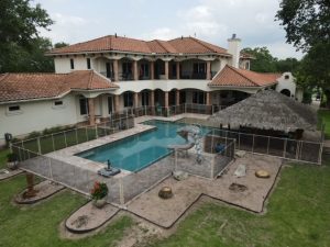 Mesh pool fence enclosing luxury geometric pool with slide and tiki hut in Houston, TX