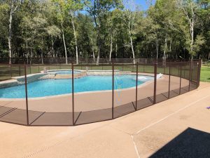 Mesh pool safety fence around a backyard swimming pool in Houston with trees in the background