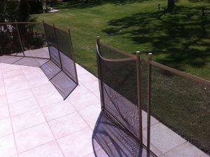 Black mesh pool fence on a tiled patio in Los Angeles, with a view of a green lawn and garden area in the background.