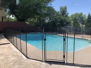 Black pool fence surrounding a swimming pool with a closed gate in Tulsa, providing safety and security.