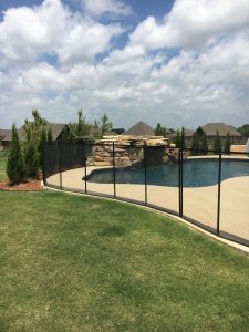 Black pool fence installed around a backyard swimming pool with rock feature, ensuring safety in a residential area in Tulsa.