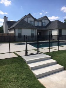 Black pool fence installed around a backyard swimming pool with a gate and steps leading up to the pool area in Tulsa.