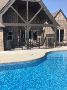 Pool fence installed on the patio of a residential property in Tulsa, with a clear view of the swimming pool and brick house.