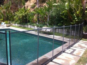 Pool in Los Angeles backyard with a black mesh safety fence, surrounded by lush greenery and tropical plants for aesthetic appeal.