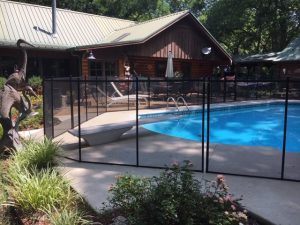 Black safety pool fence enclosing a swimming pool with a ladder next to a garden with flowers and a wooden house in Tulsa.