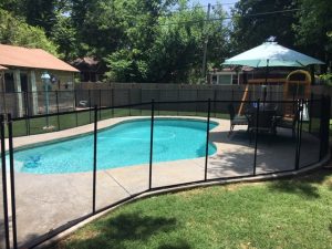Safety fence for pool in Tulsa backyard with curved fence, play area, and outdoor dining set under an umbrella.