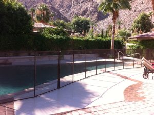 Pool in Los Angeles with a black mesh fence, lush greenery, a palm tree, and a mountain view in the background.