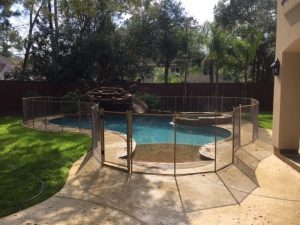 Tan mesh secure pool fence installation in Houston with self-closing gate and natural rock waterfall pool