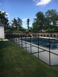 Black mesh pool fence installed around a backyard swimming pool with a playground in the background in Tulsa.