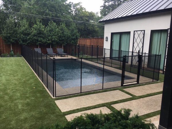 A rectangle pool in altamonte springs surrounded by a black mesh pool fence surrounded by grass and other backyard features.