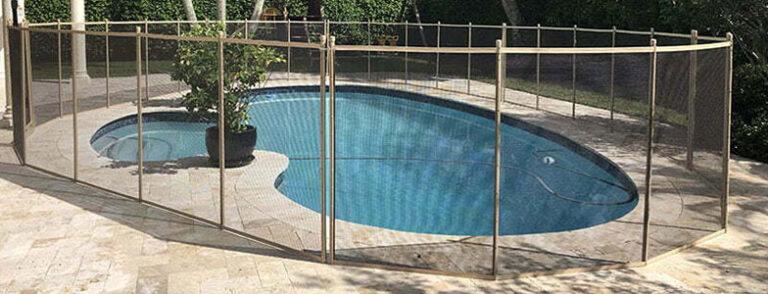 A kidney-shaped pool in upper florida keys surrounded by a beige mesh pool fence with a potted plant placed near the water. The fence is positioned securely around the pool, with a safety barrier, and plants visible in the background.