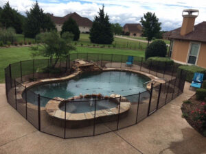 Black mesh pool fence installed around a uniquely shaped pool with attached spa in Dallas backyard