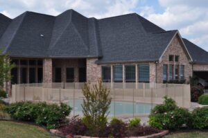 Luxury beige pool fence surrounding a modern backyard swimming pool in Dallas with brick home in the background