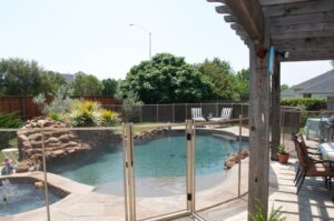 White mesh pool fence installed around a freeform swimming pool with a waterfall feature in a Dallas backyard