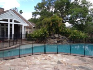 Black mesh pool safety fence installed around a pool with a rock waterfall in Berkeley, California