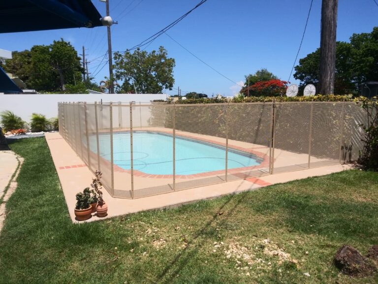 Beige mesh pool safety fence installed around a rectangular backyard pool in a tropical Bahamian setting
