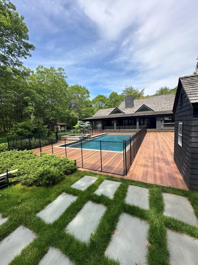 Black mesh pool safety fence installed around a rectangular backyard pool with wooden decking in Canada