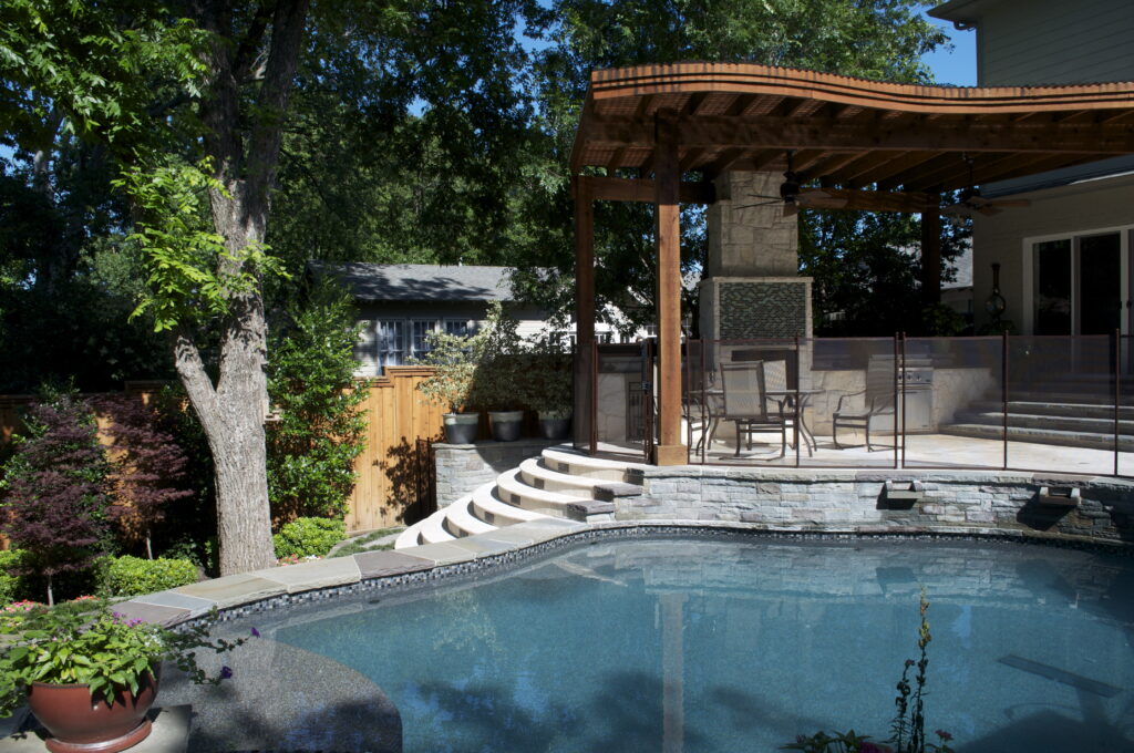 Elegant mesh pool fence installed around a raised backyard patio and pool area with modern landscaping and outdoor seating in a San Diego home.