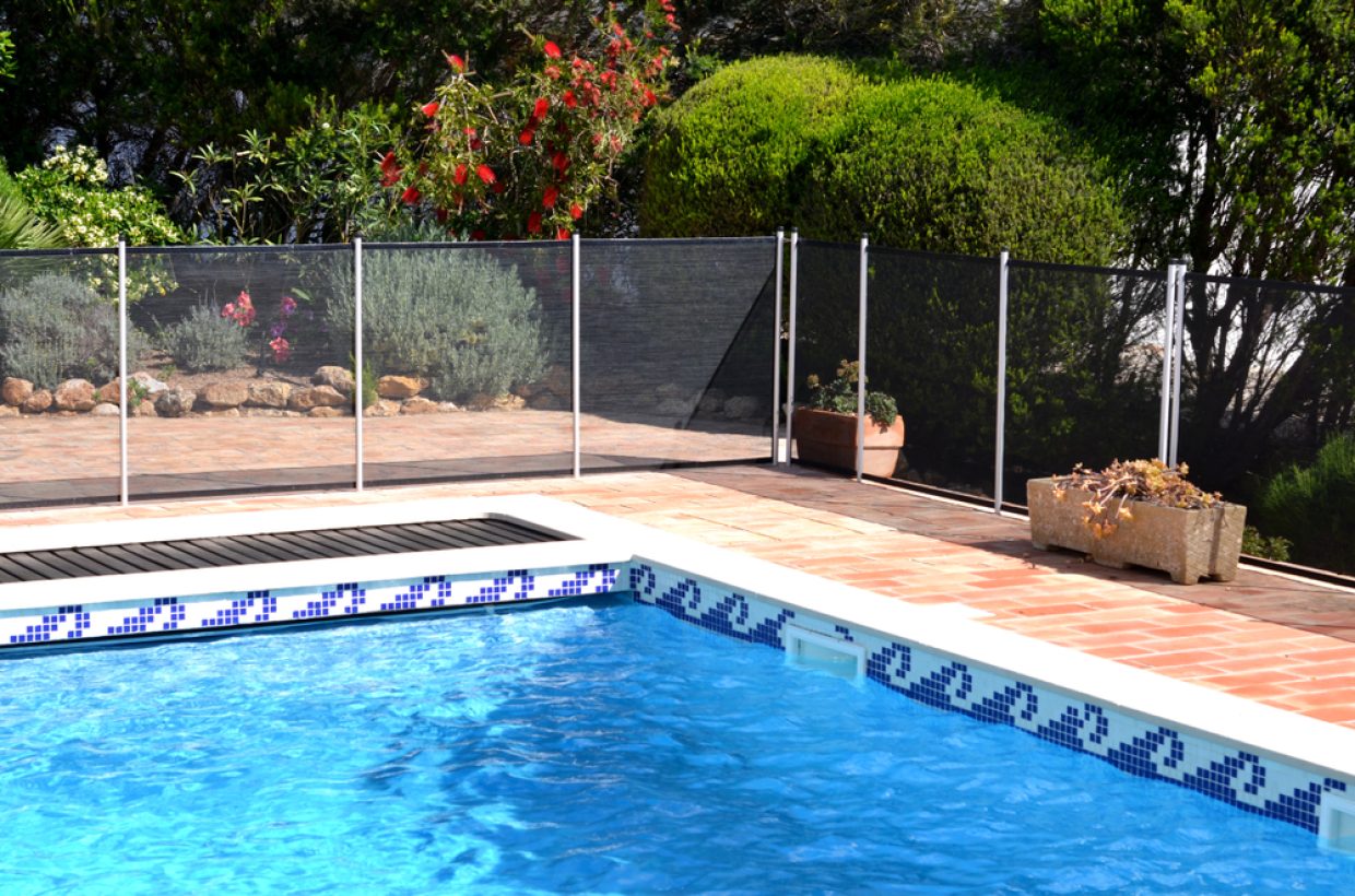 Pool safety fence around pool with blue wave pattern tile and garden in